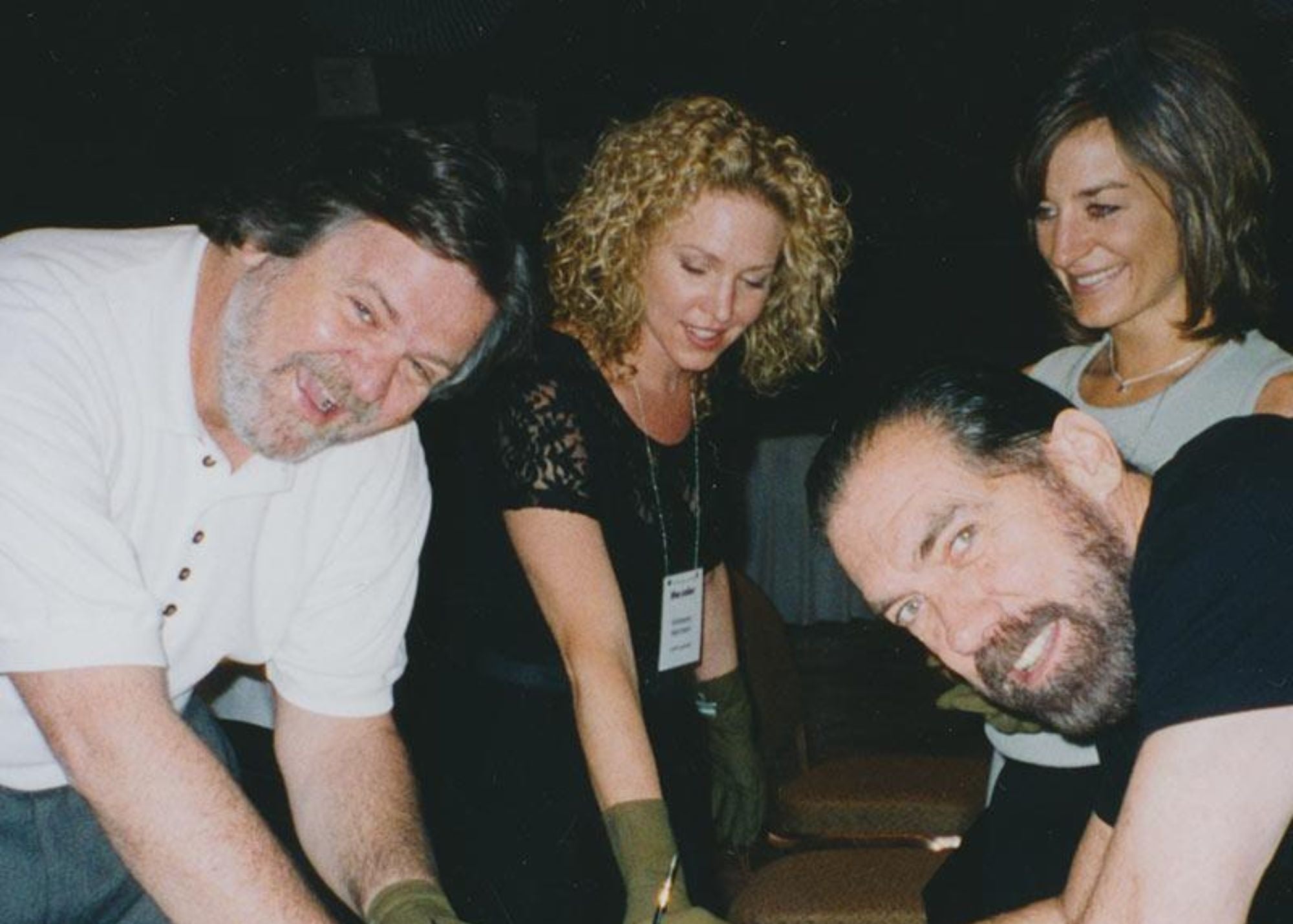 Four people posing together in a casual setting with dark background