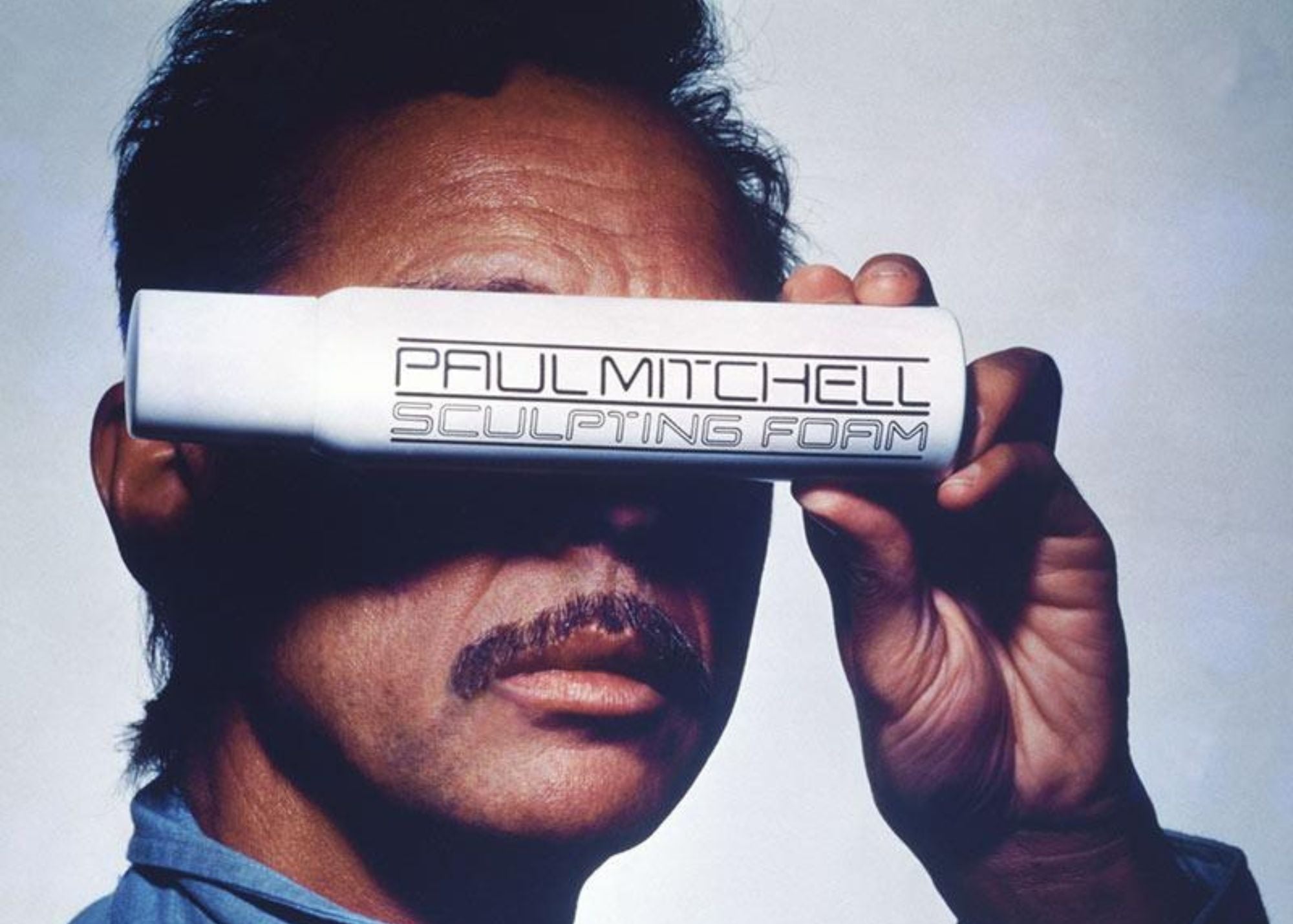 Paul Mitchell holding one of the original sculpting foam bottles in front of his eyes
