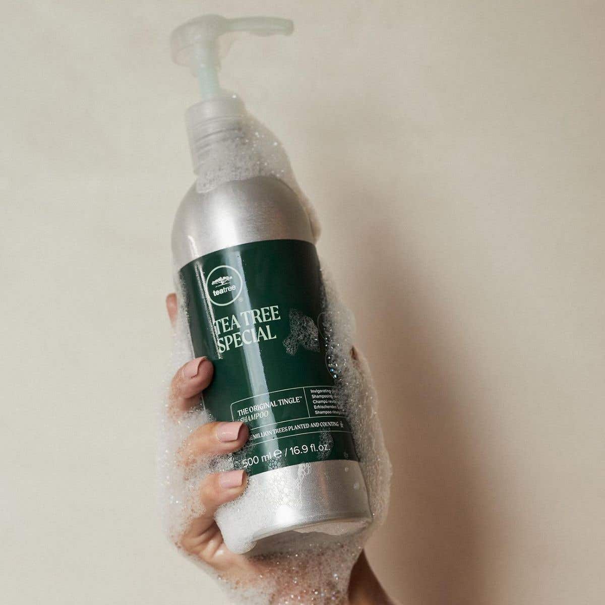 Image of someone holding Tea Tree Special Shampoo Aluminum Bottle with suds all over it