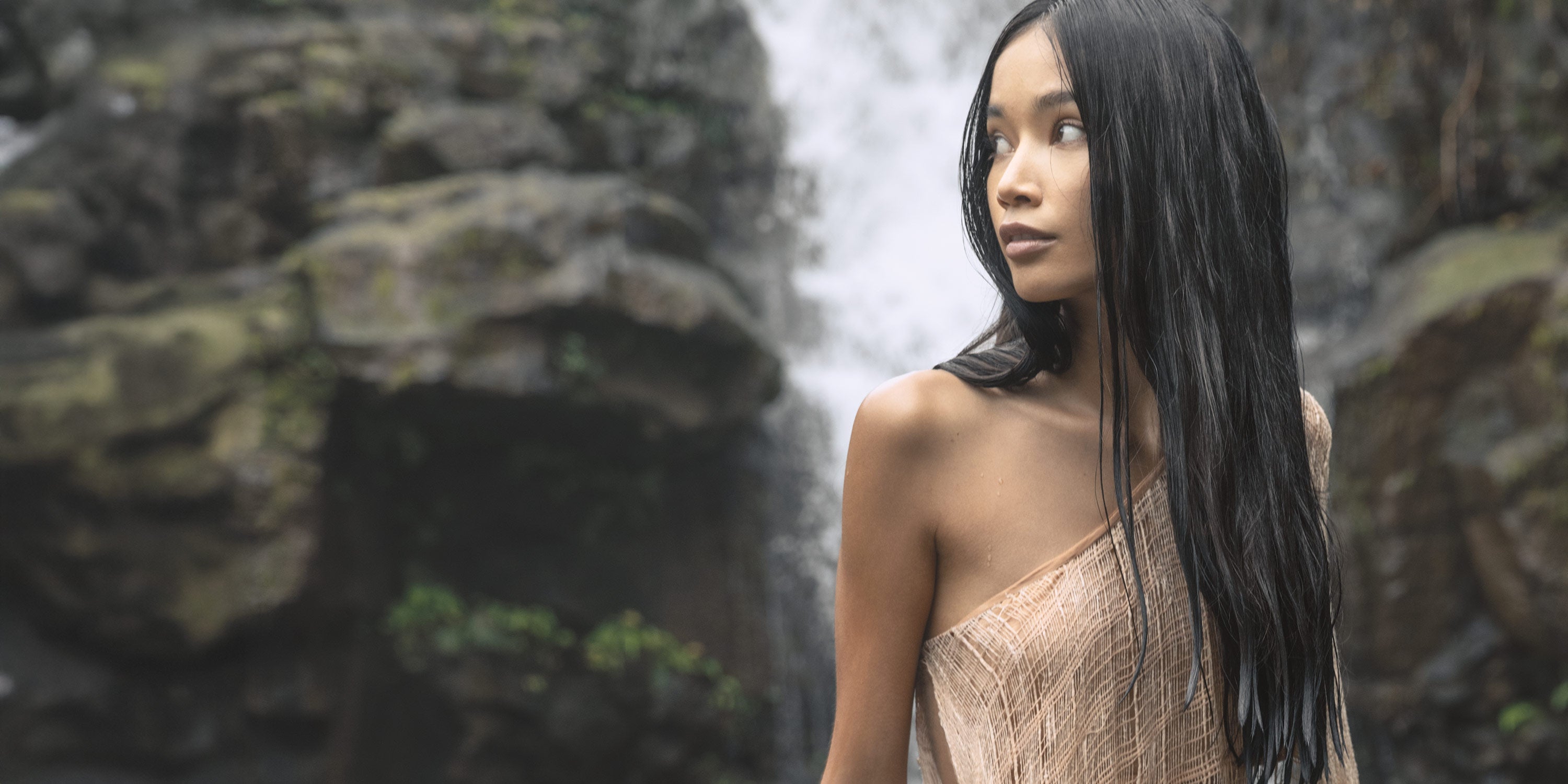 Woman in a flowing dress standing in front of a waterfall