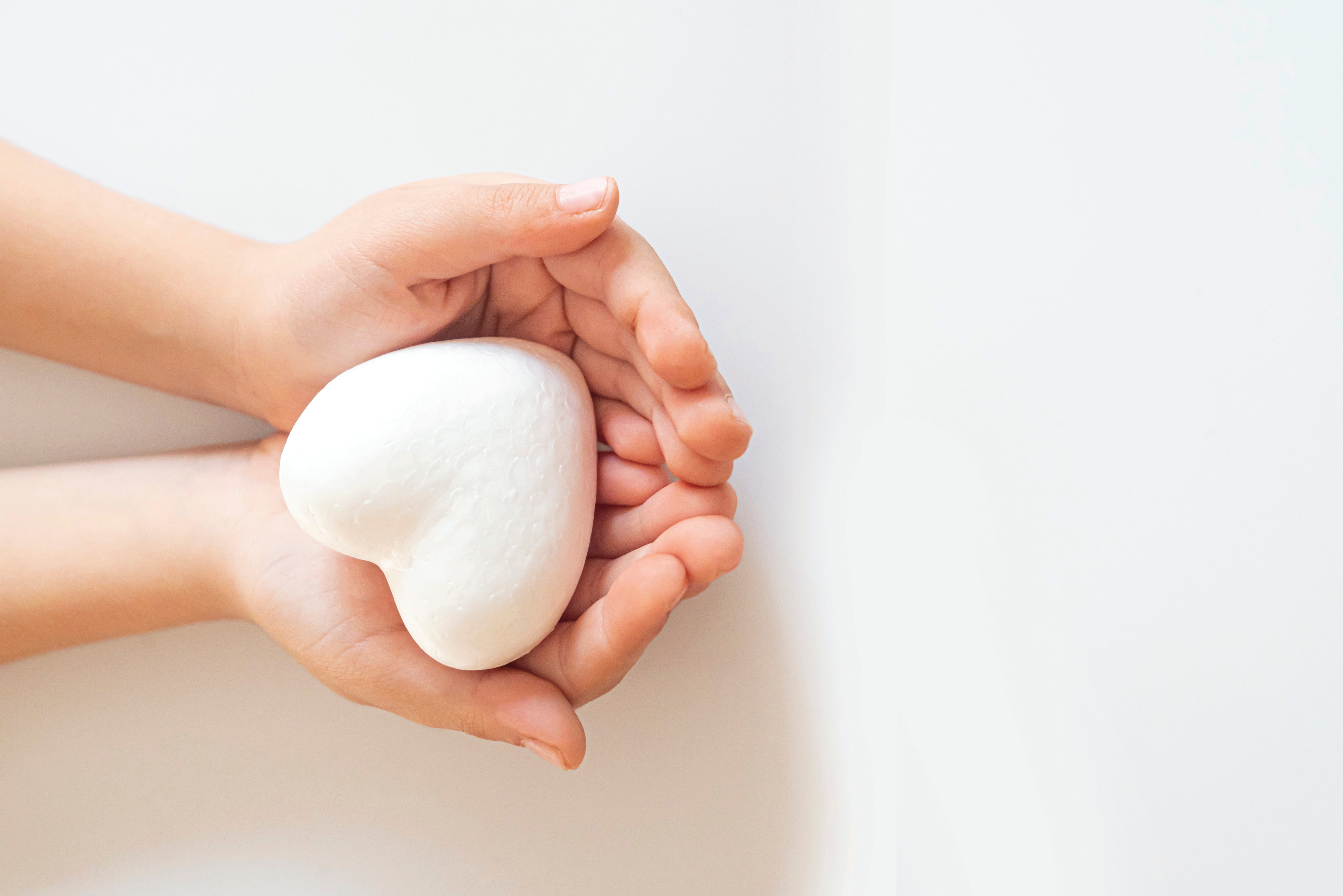 Two hands holding a heart-shaped object against a light background