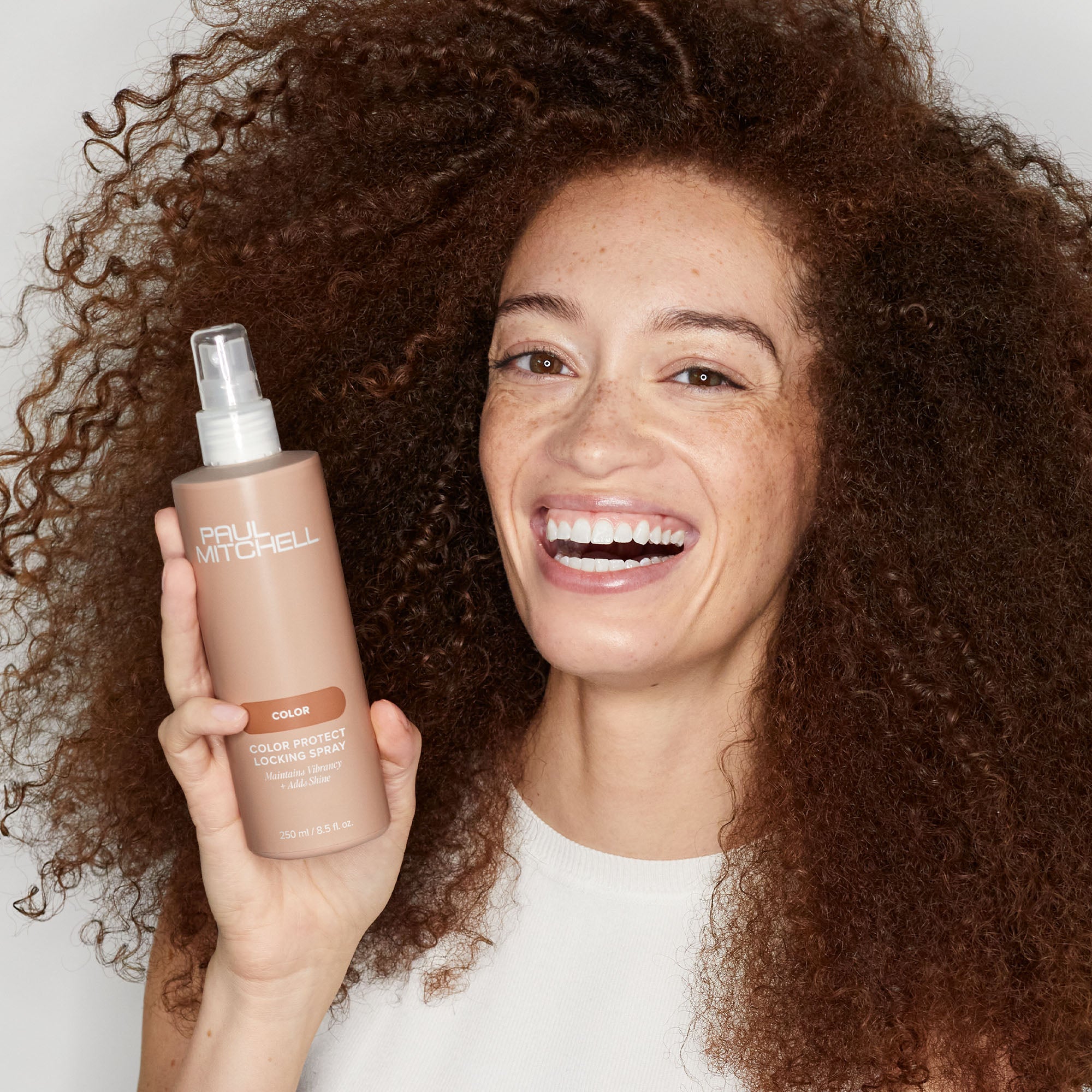 Image of Paul Mitchell Color model holding spray bottle of Color Protect Locking Spray near their face