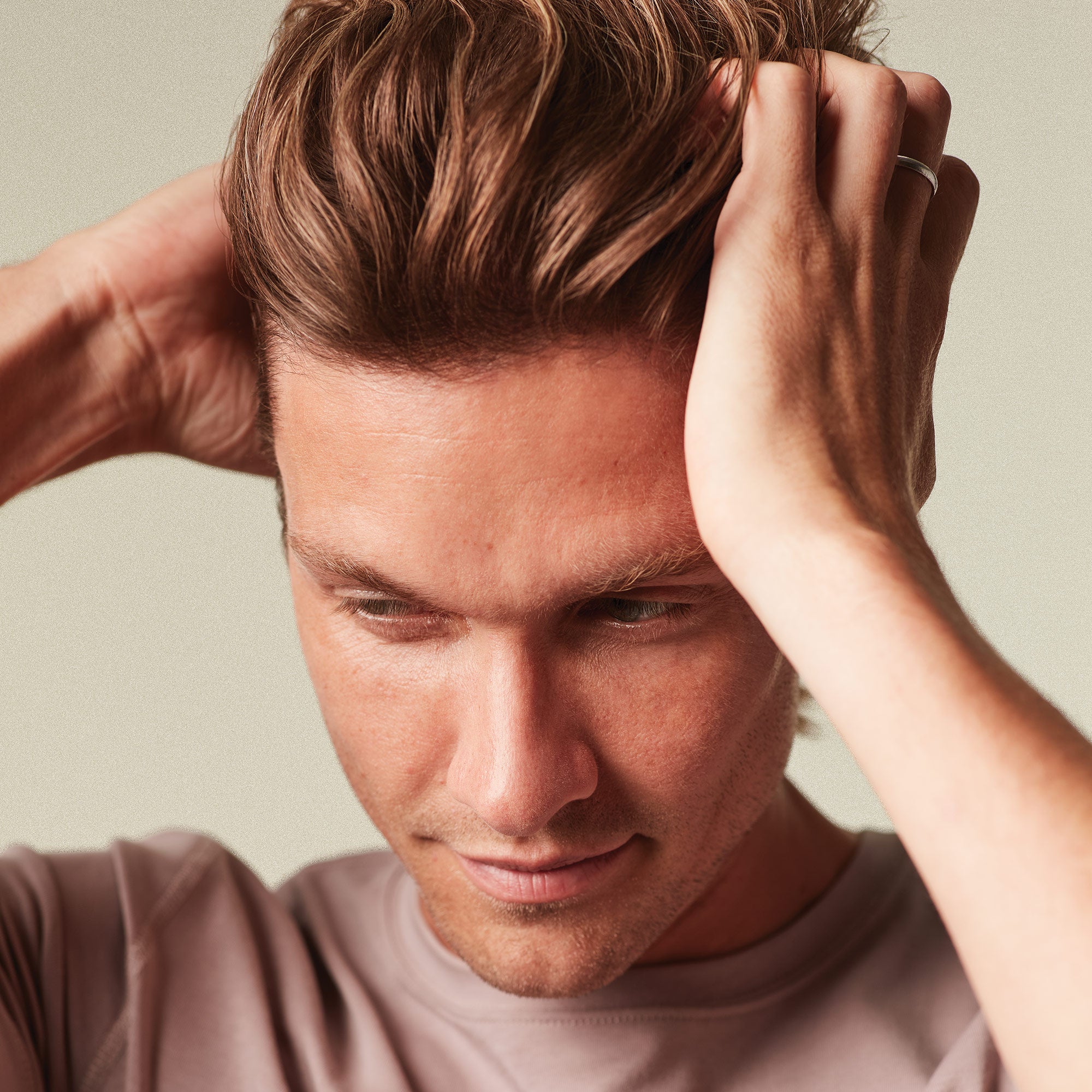 Man adjusting his hair against a neutral background