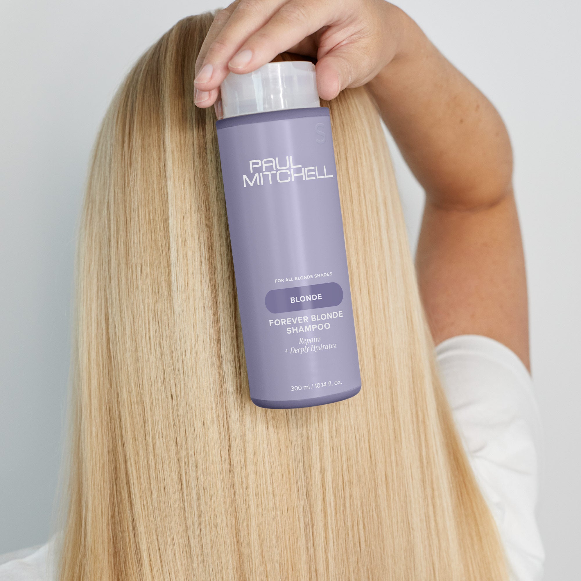Image of model with blonde smooth hair holding bottle of Forever Blonde Shampoo on the back of their head
