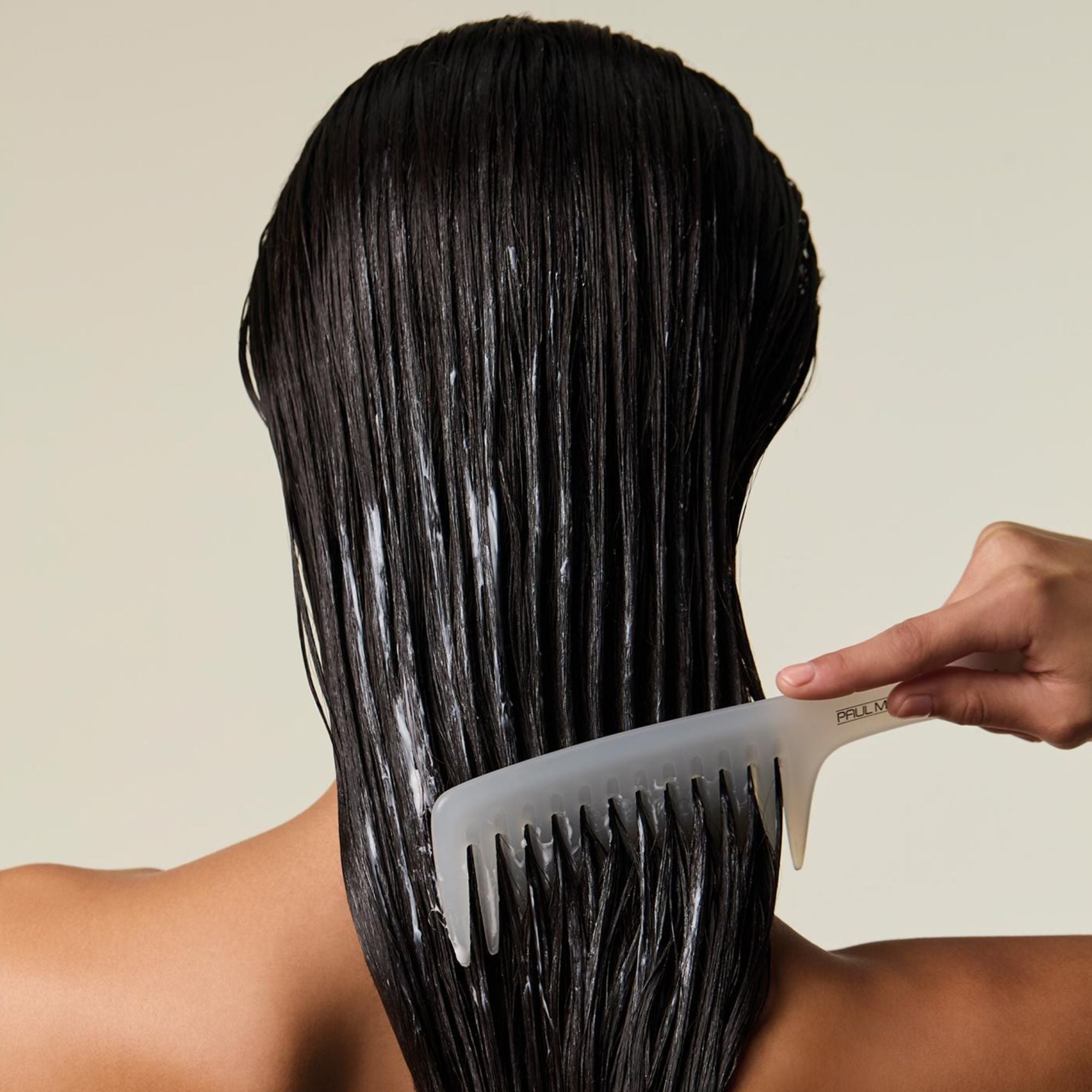 Female applying hair mask to wet hair with Detangler Comb, against a neutral background