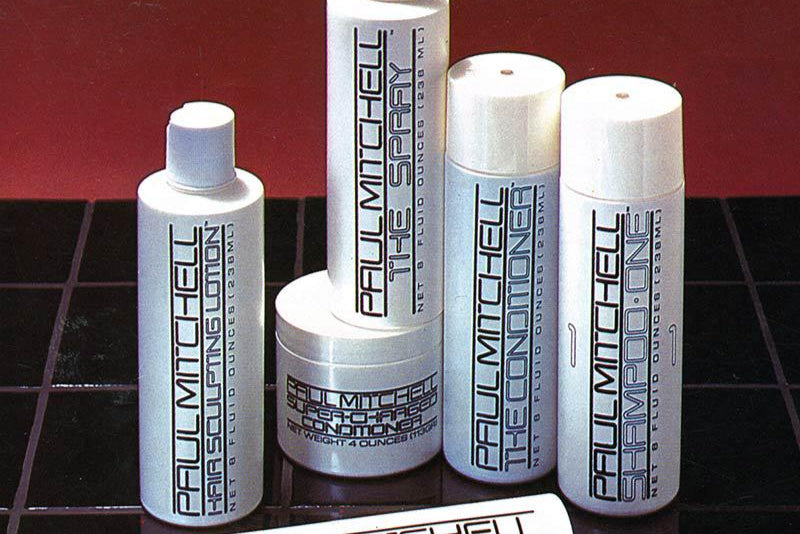 Set of original Paul Mitchell hair care products including shampoo, conditioner, lotion, and spray on a black grid and red background