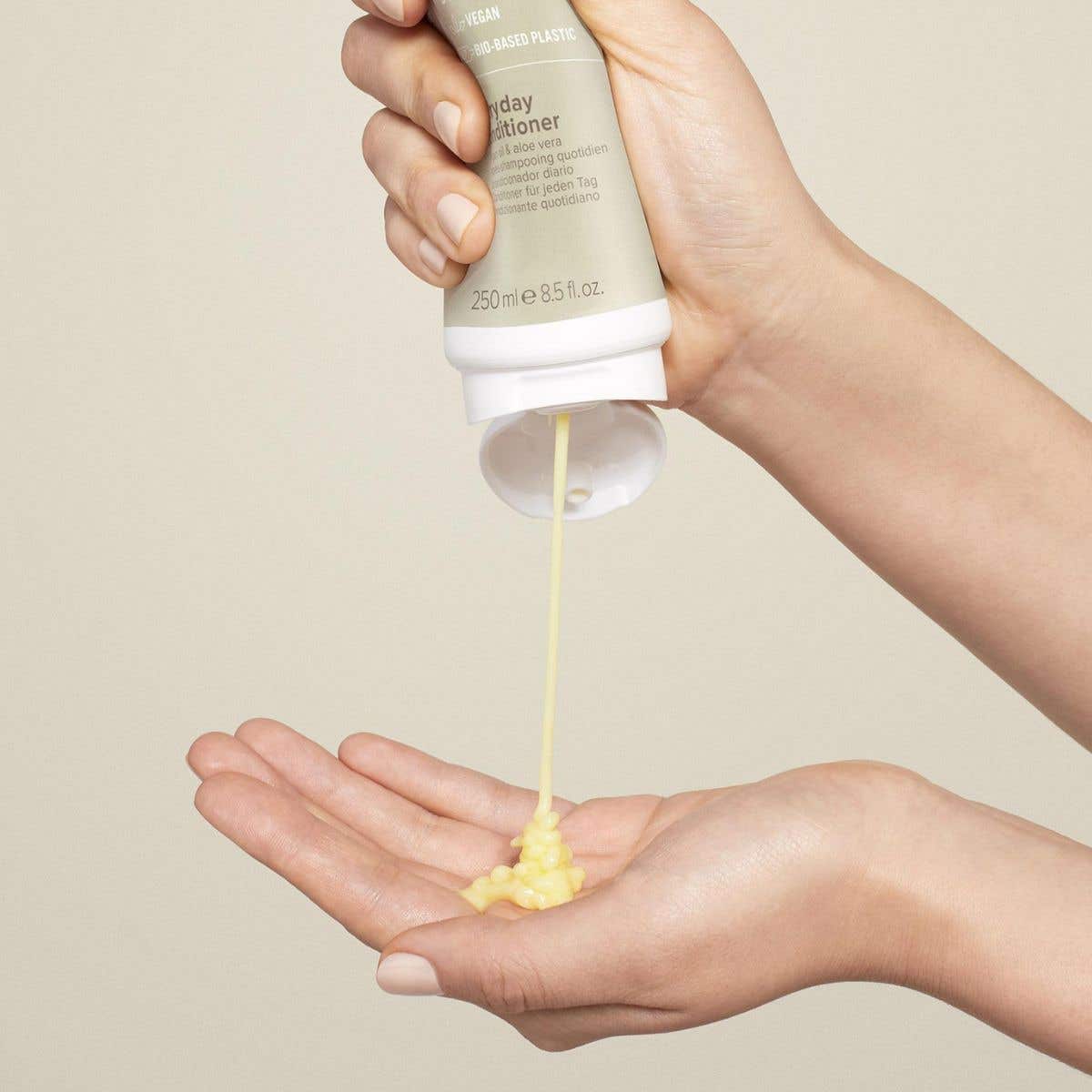 An image of someone dispensing Everyday Conditioner into their hands on a soft cream background