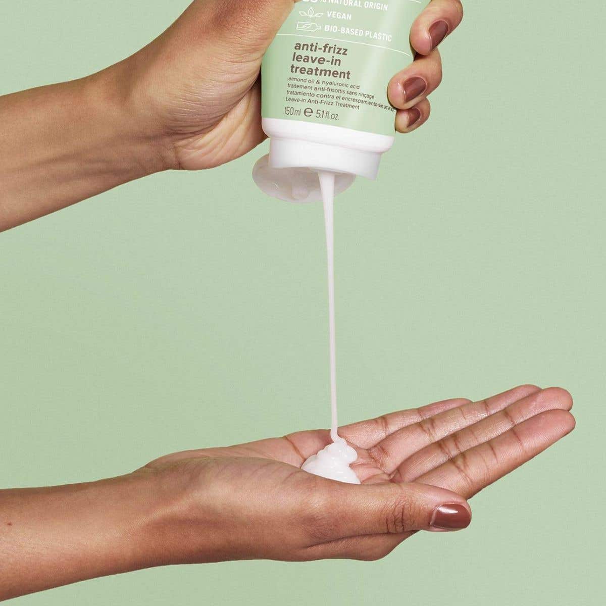 An image of someone dispensing Anti-Frizz Leave-In Treatment into their hands on a soft green background