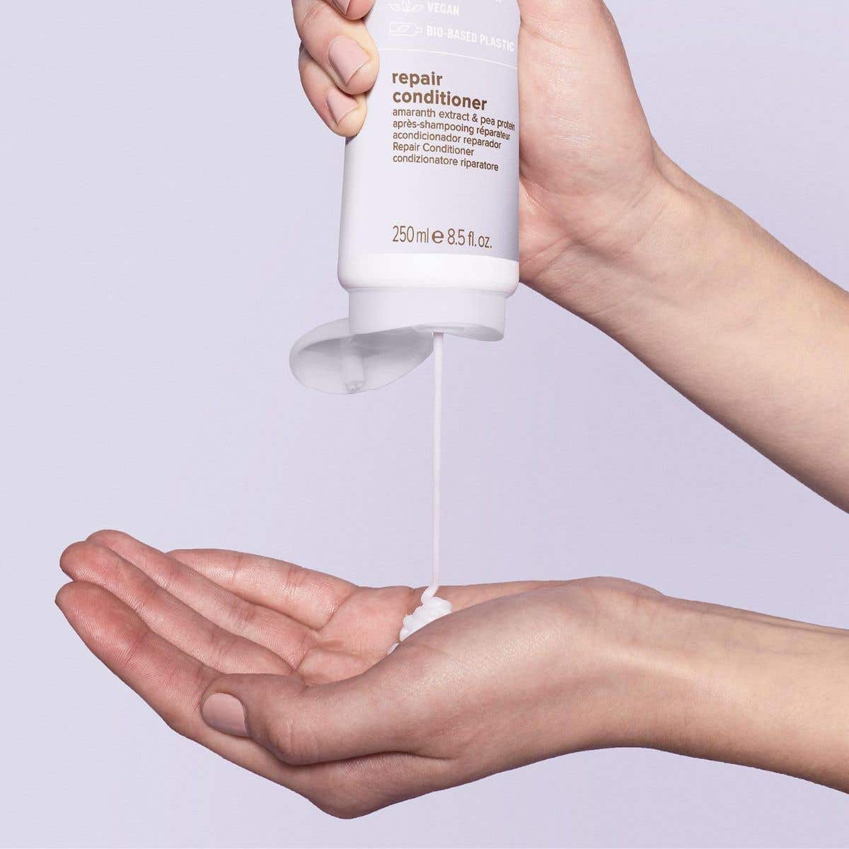 Image of someone dispensing Repair Conditioner into their hands over a soft purple background