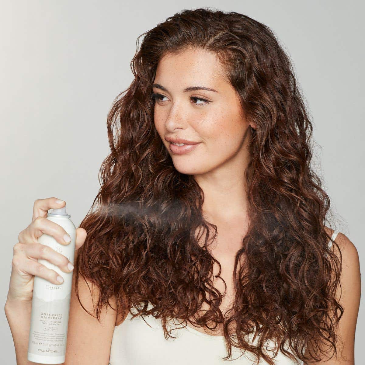 Image of Wapuhi Wild Ginger model spraying Anti-Frizz Hairspray on the ends of her hair