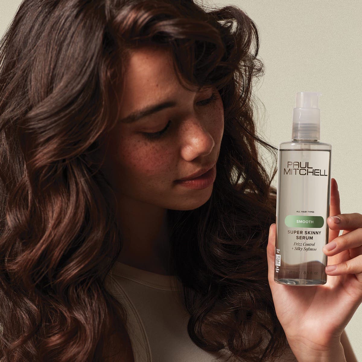 Paul Mitchell model with shiny wavy frizz free hair holding bottle of Super Skinny Serum near their face