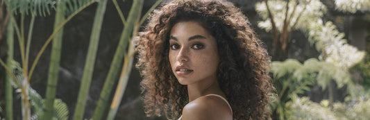 image of a woman with curly, brunette hair posing in a rainforest