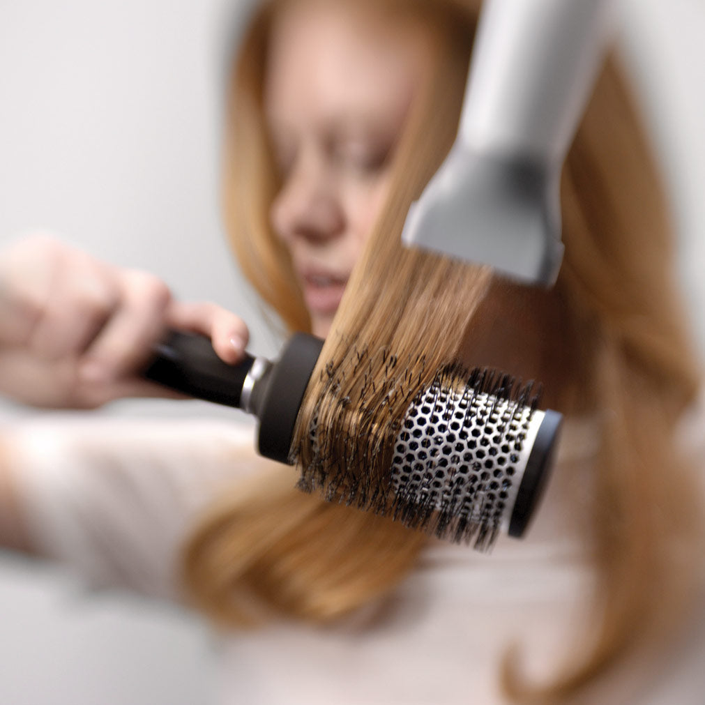 Person using a hair dryer and round brush on their hair