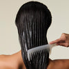 Female applying hair mask to wet hair with Detangler Comb, against a neutral background