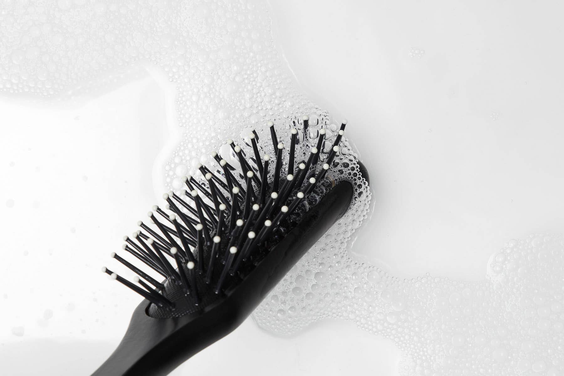 A hairbrush getting clean in water with a cleansing or clarifying shampoo.