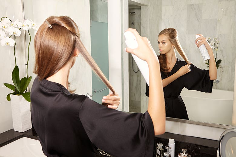 Marula How-To: Glamorous Waves Step 2 of 11. Woman spraying sections of hair with Rare Oil Perfecting Hairspray.