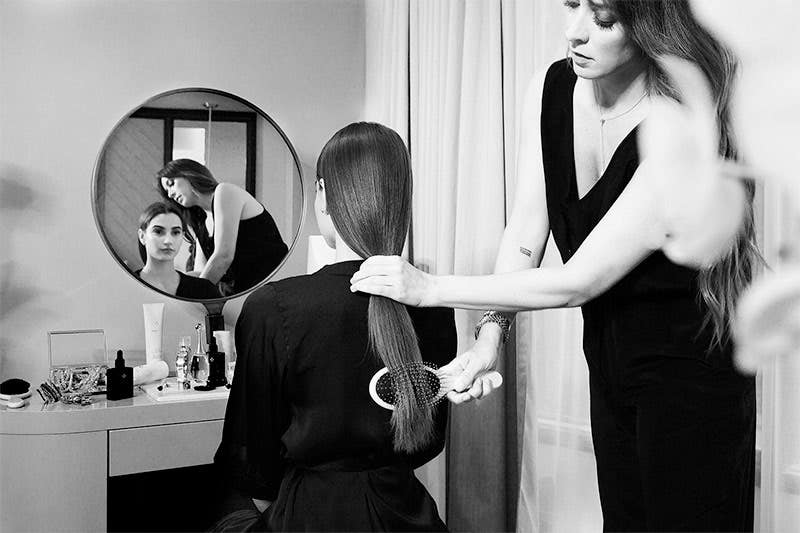 Step one, model is sitting at a mirror while a stylist brushes out her hair