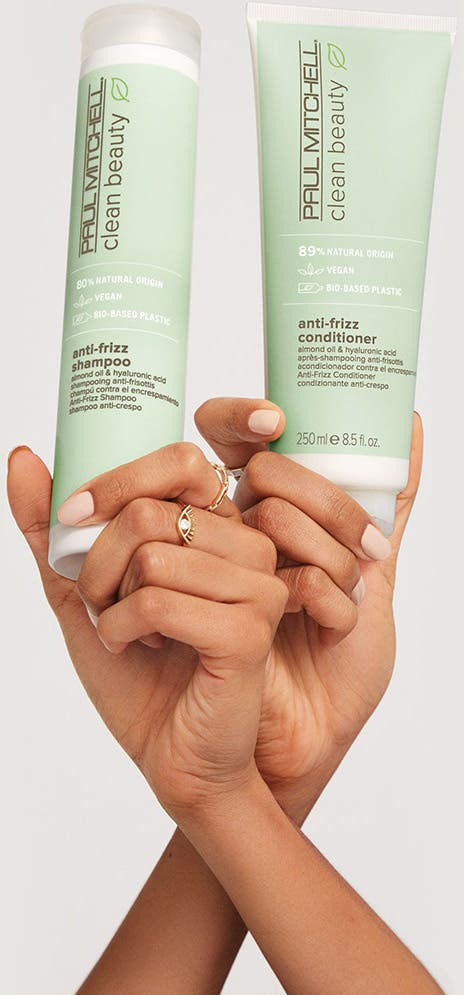 crossed arms holding Clean Beauty Anti-Frizz Shampoo and Conditioner bottles